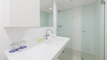Un baño moderno con un lavamanos blanco, un espejo grande y una cabina de ducha de vidrio.