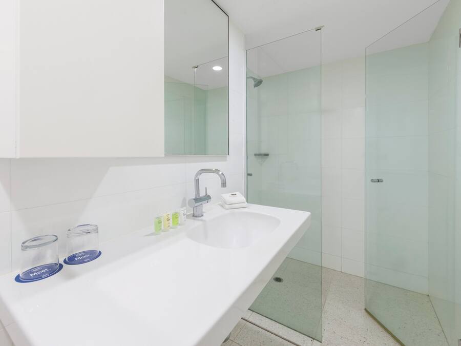 Un baño moderno con un lavamanos blanco, un espejo grande y una cabina de ducha de vidrio.