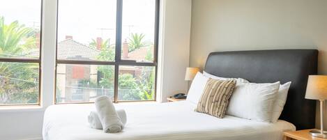 Una habitación de hotel con una cama grande, dos lámparas de noche y un ventanal con vistas a edificios y áreas verdes.
