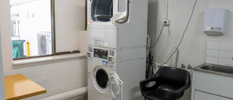 A compact laundry room with a stacked washer and dryer, a small sink, and a chair.
