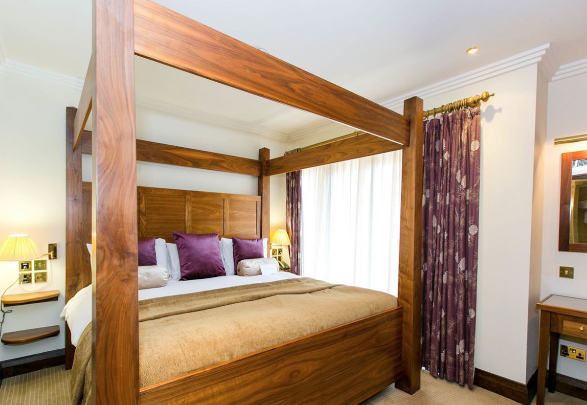 Una cama con dosel de madera, cabecera y colcha.