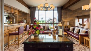 Amplia sala de estar con una mesa de centro de vidrio, un candelabro y vistas a una casa a través de grandes ventanales.