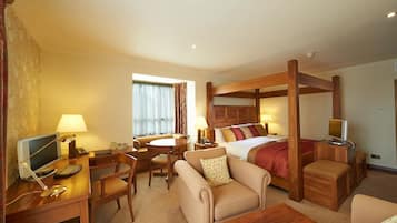 A hotel room with a four-poster bed, a desk with a computer, a sofa, and a TV.
