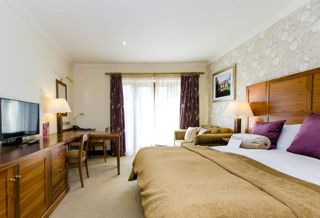 A hotel room with a bed, a desk, a television, and a window with curtains.
