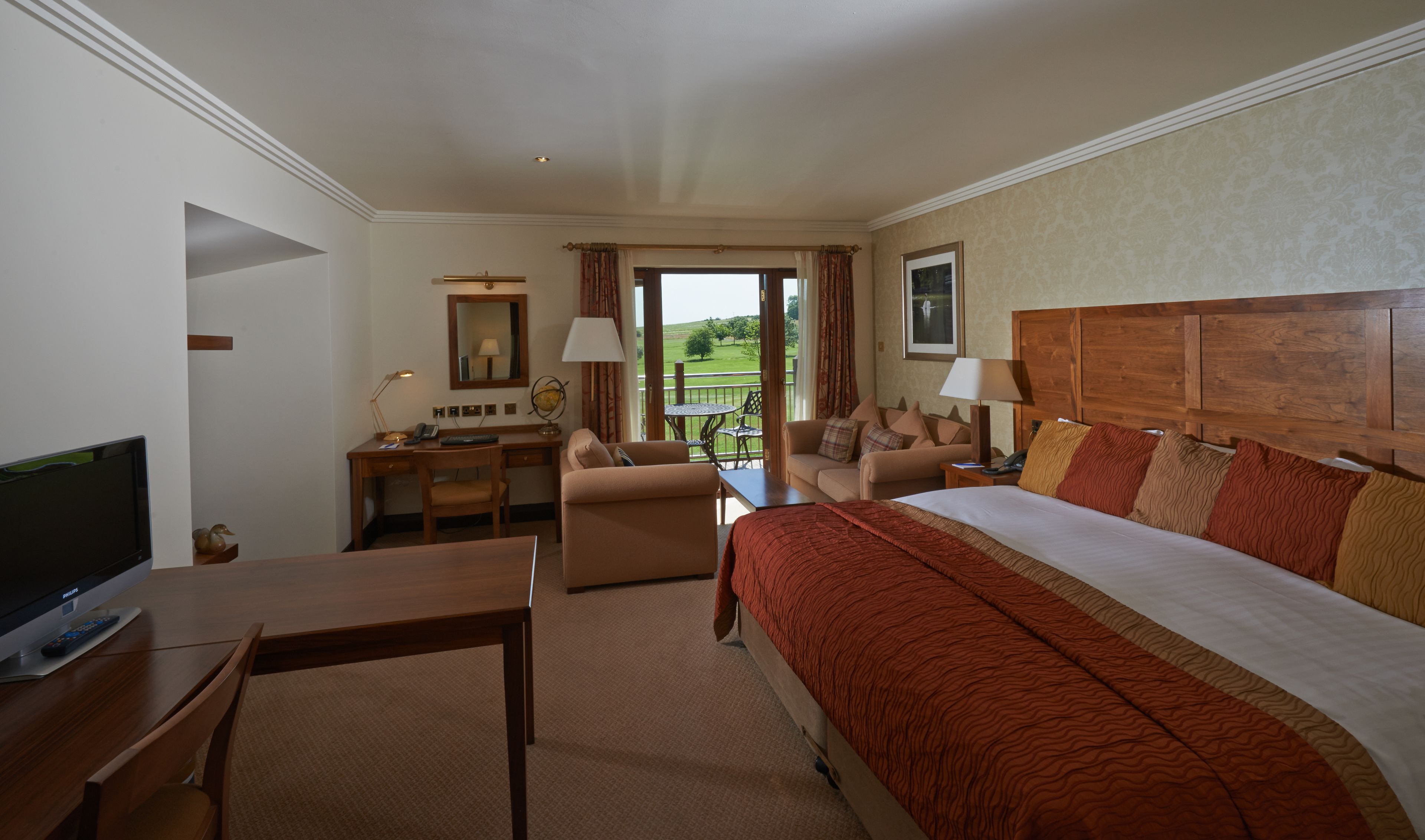 A hotel room with a bed, a desk, a television, and a view of the outdoors.