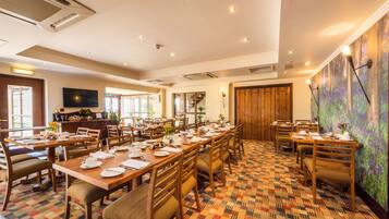 A dining area with multiple tables set for meals, a television mounted on the wall, and a patterned carpet.