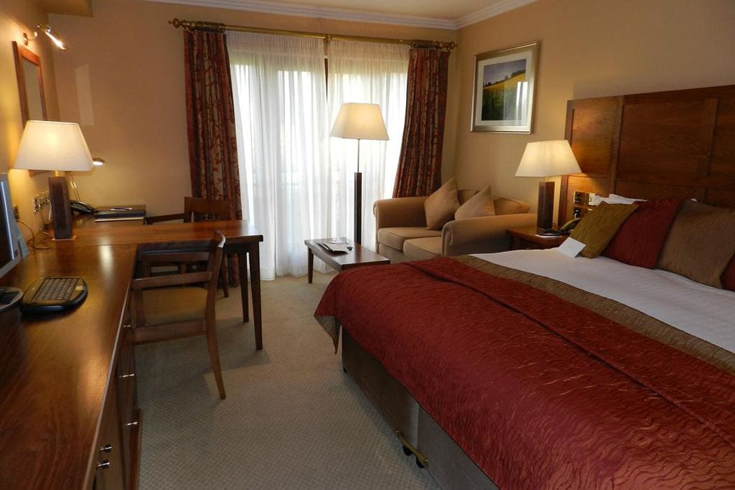 Habitación de hotel con cama, escritorio con silla, sofá y dos lámparas.