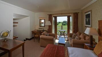 A hotel room with a bed, two armchairs, a small table, a desk, and a balcony with a view of the garden.