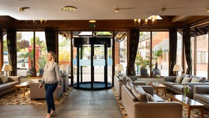 Un vestíbulo de hotel con una puerta giratoria, sofás y una alfombra estampada.