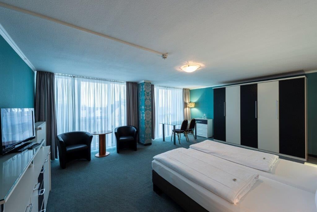 A hotel room with a bed, a desk, a chair, a TV, and a wardrobe.