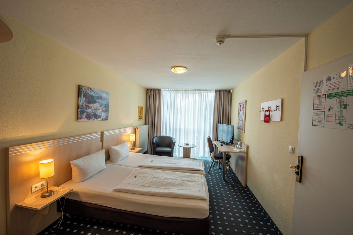 A hotel room with two beds, a desk with a chair, a TV, and a window with curtains.