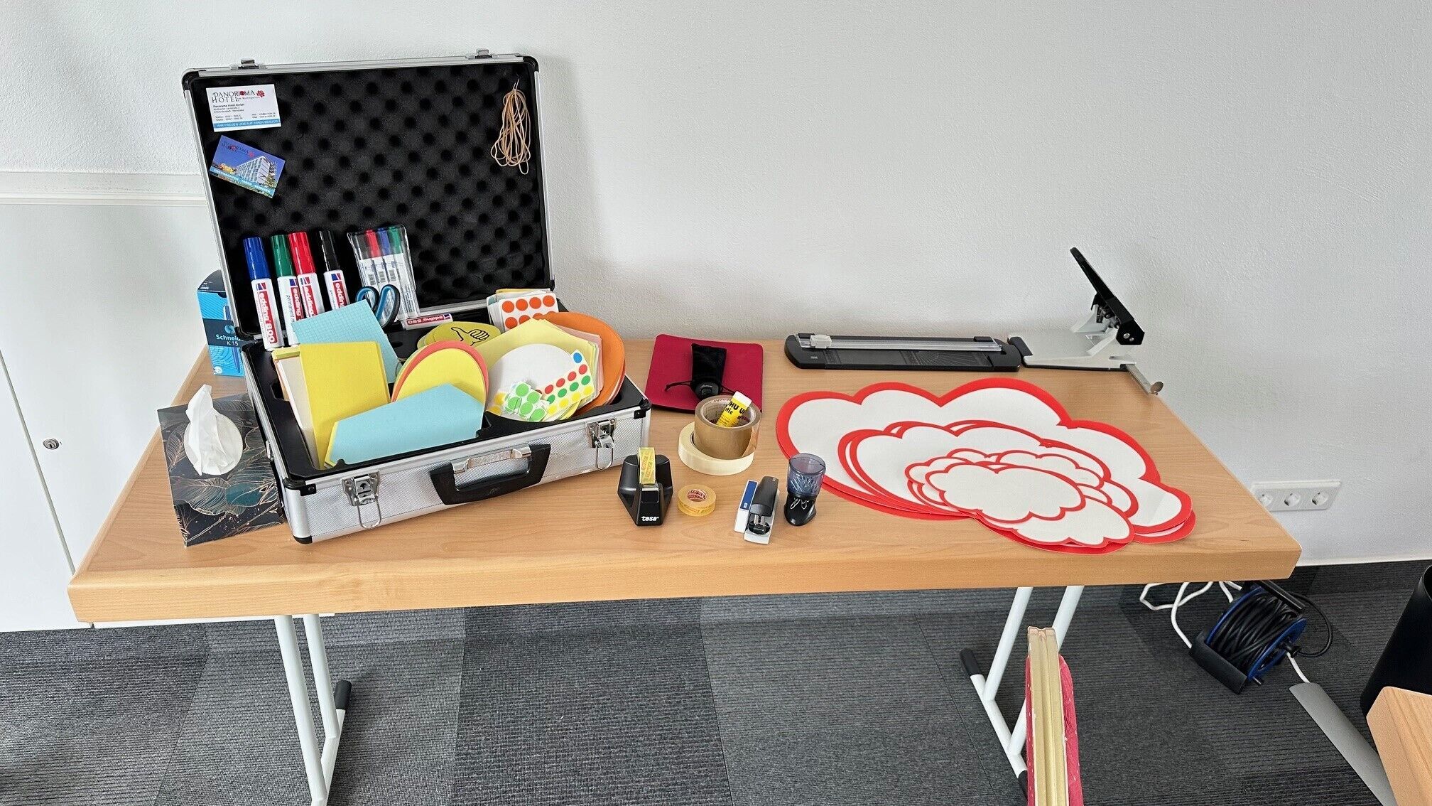 A workspace with a suitcase containing stationery, a cutting mat, and a laser cutter.