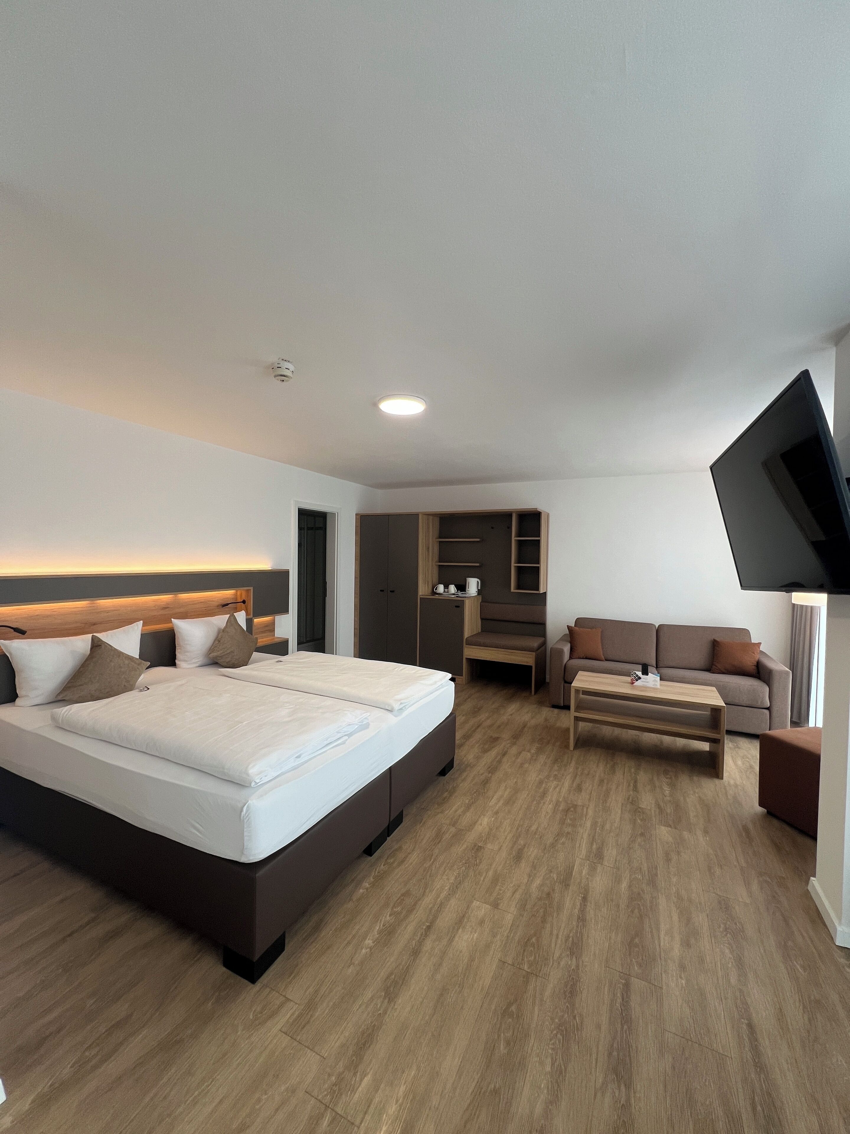 Ein modernes Hotelzimmer mit einem großen Bett, einer Couch, einem Couchtisch und einem an der Wand befestigten Fernseher.