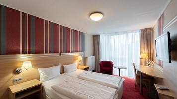 Habitación de hotel con dos camas, un escritorio, una silla, un televisor y una ventana con cortinas.