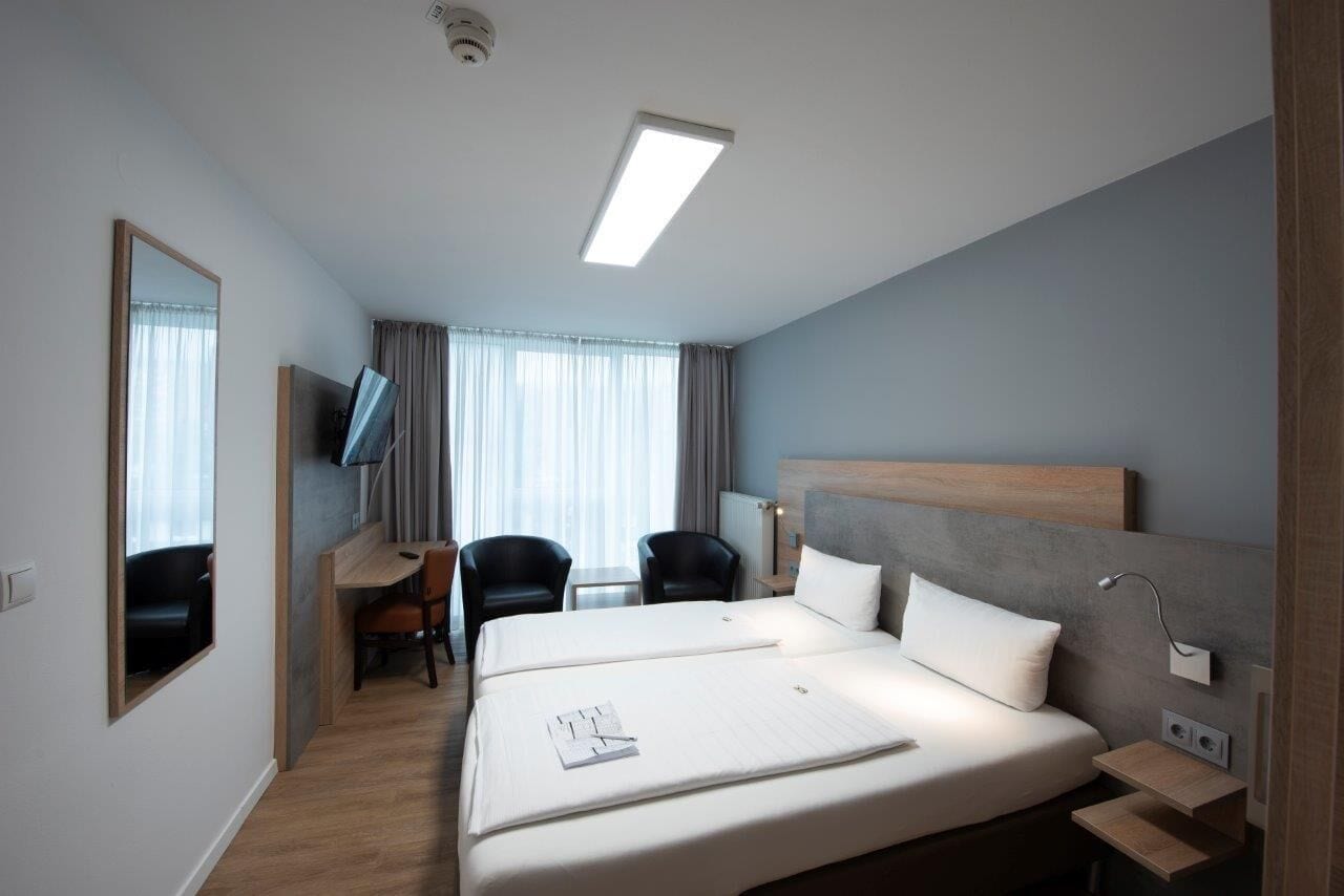 A hotel room with a large bed, a desk with a chair, a TV, and a window with curtains.