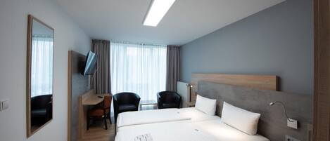A hotel room with a large bed, a desk with a chair, a TV, and a window with curtains.