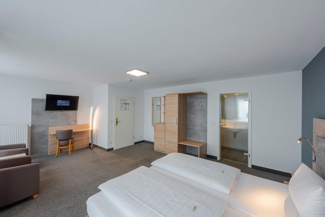A hotel room with a bed, a desk, a chair, a wardrobe, and a television on the wall.