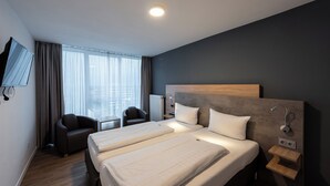 Ein Hotelzimmer mit zwei Betten, einem Fernseher, einem Schreibtisch und Blick auf die Stadt.