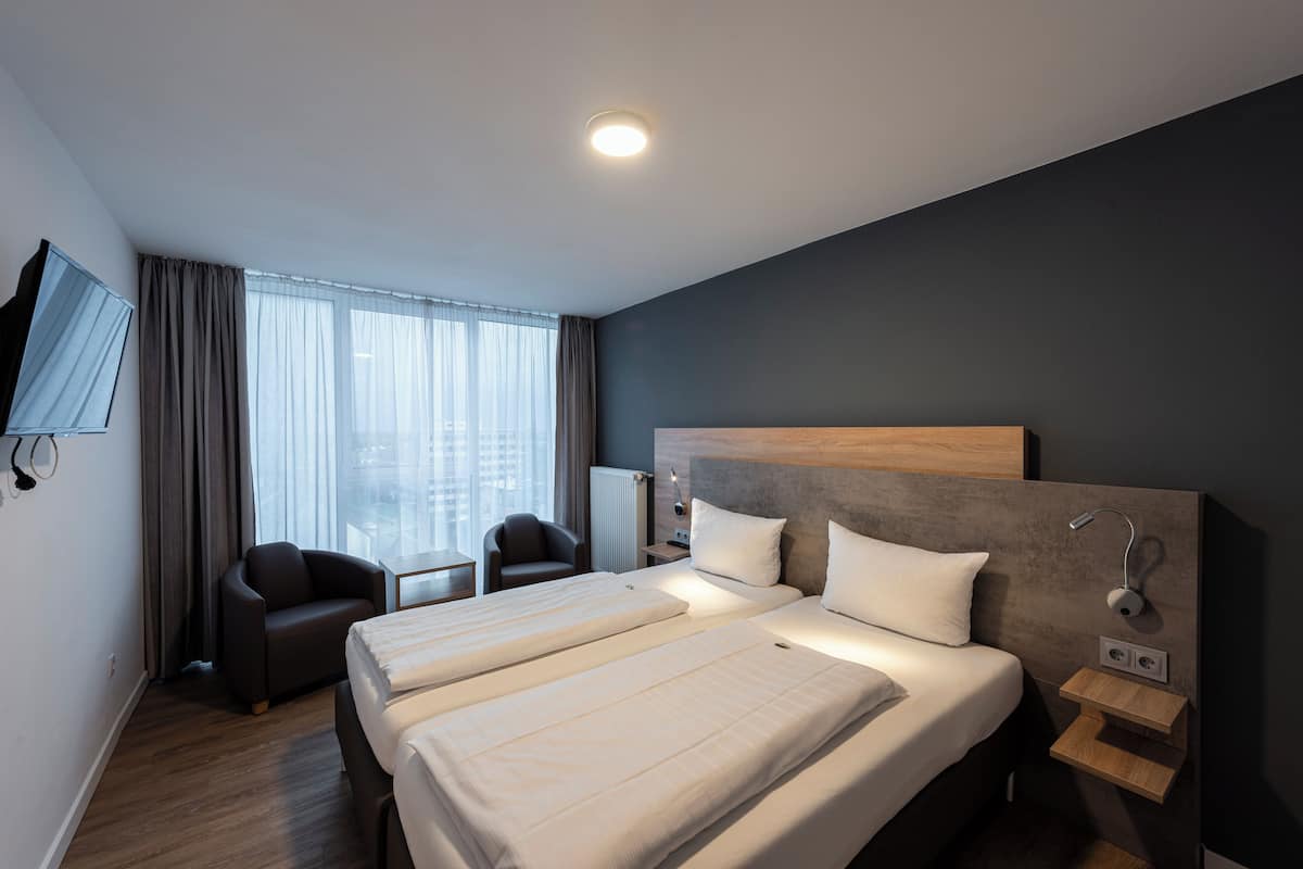 A hotel room with two beds, a TV, a desk, and a view of the city.