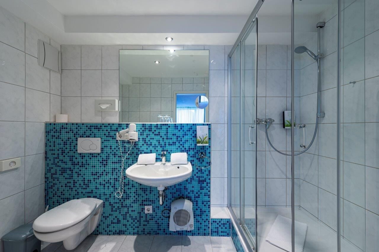Ein modernes Badezimmer mit blauer Mosaikfliesenwand, einem weißen Waschbecken, einer Toilette und einer Duschkabine.