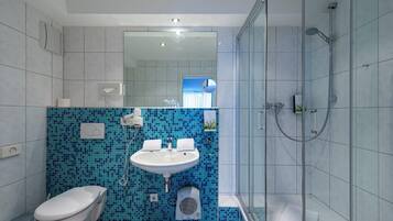 Ein modernes Badezimmer mit blauer Mosaikfliesenwand, einem weißen Waschbecken, einer Toilette und einer Duschkabine.