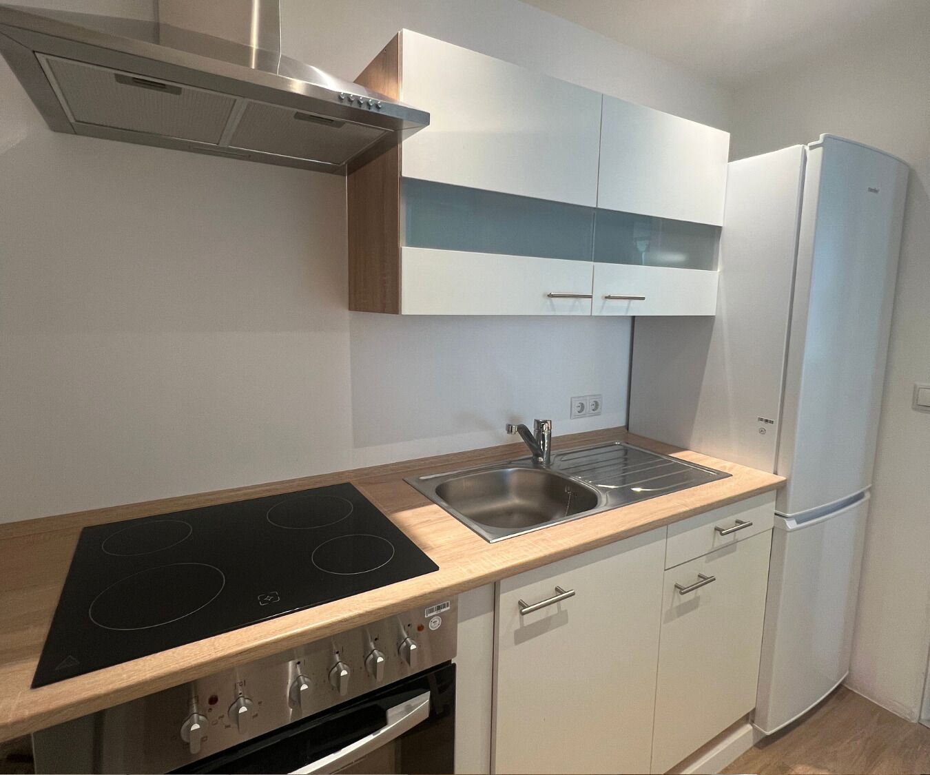 A modern kitchen with a black induction cooktop, stainless steel sink, white cabinets, and a built-in oven.