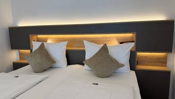 A neatly made bed with white bedding and two pillows, a wooden headboard with integrated lighting, and a small bedside table.