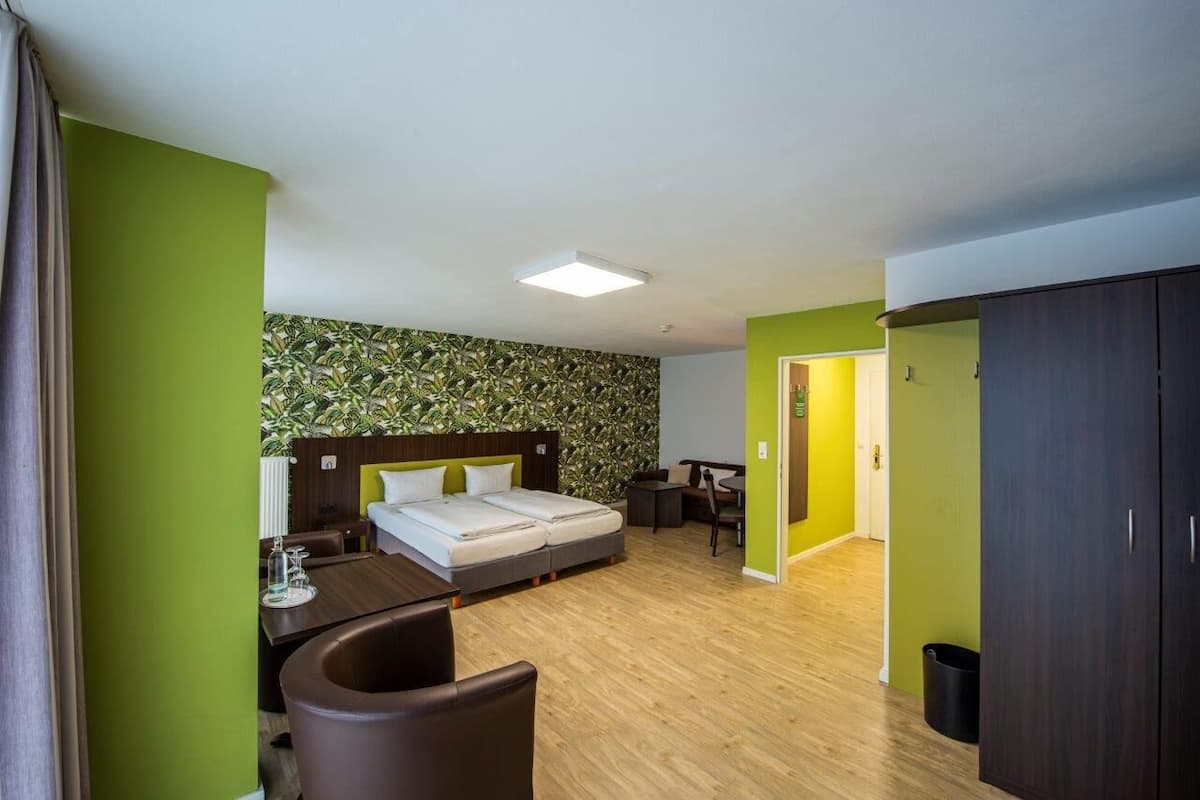 A hotel room with a bed, a desk, a chair, a trash bin, and a wardrobe.