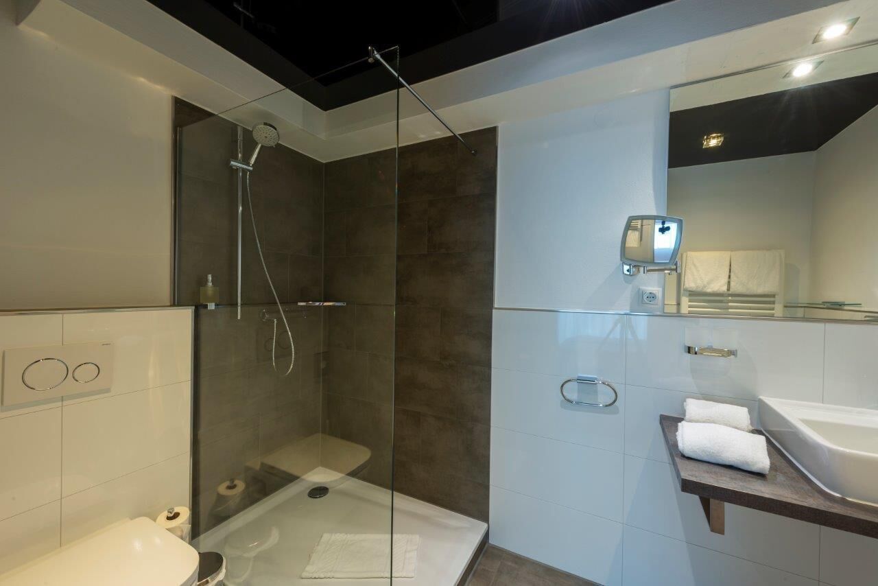 Une salle de bain moderne avec une douche à parois de verre, un lavabo blanc et un grand miroir.