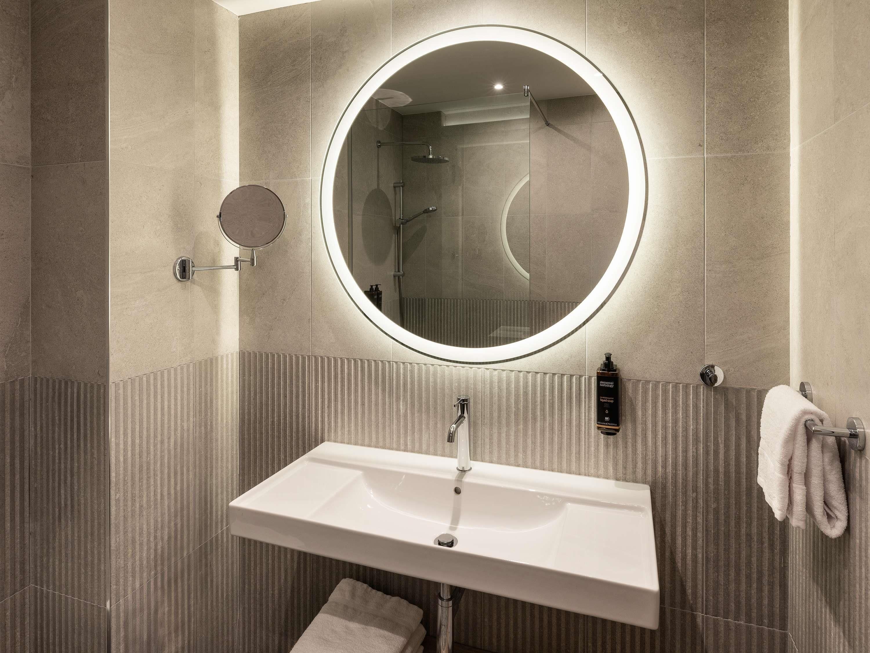 Un baño moderno con un espejo redondo, un lavamanos rectangular y un perchero para toallas.