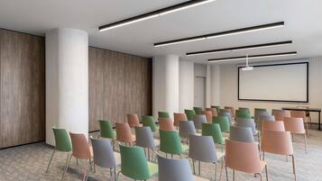 Una sala conferenze con file di sedie, uno schermo per proiettore e illuminazione moderna.