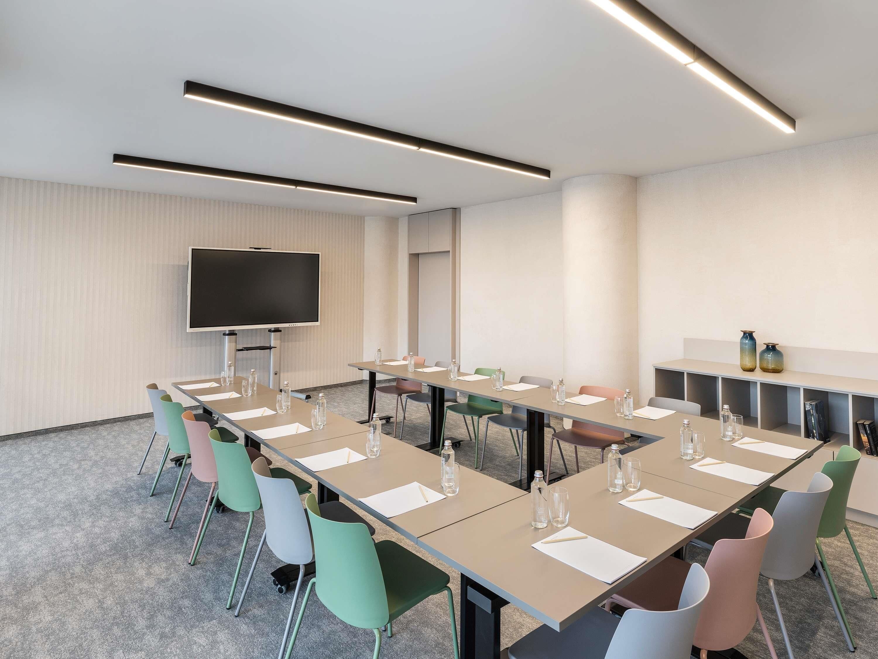 A conference room with a long table, chairs, a flat-screen TV, and a shelf with decorative items.
