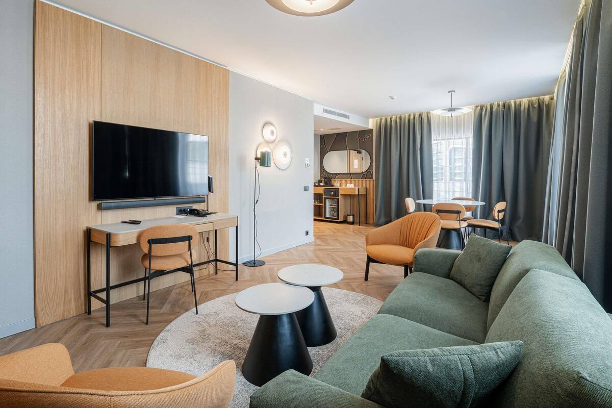 A modern living room with a flat-screen TV, a sofa, two round tables, and a dining area in the background.