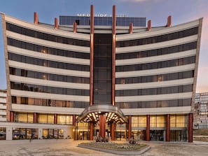 A modern hotel with a curved facade, multiple floors, and a central entrance with a canopy. - Mercure Sofia City  (Sofia)
