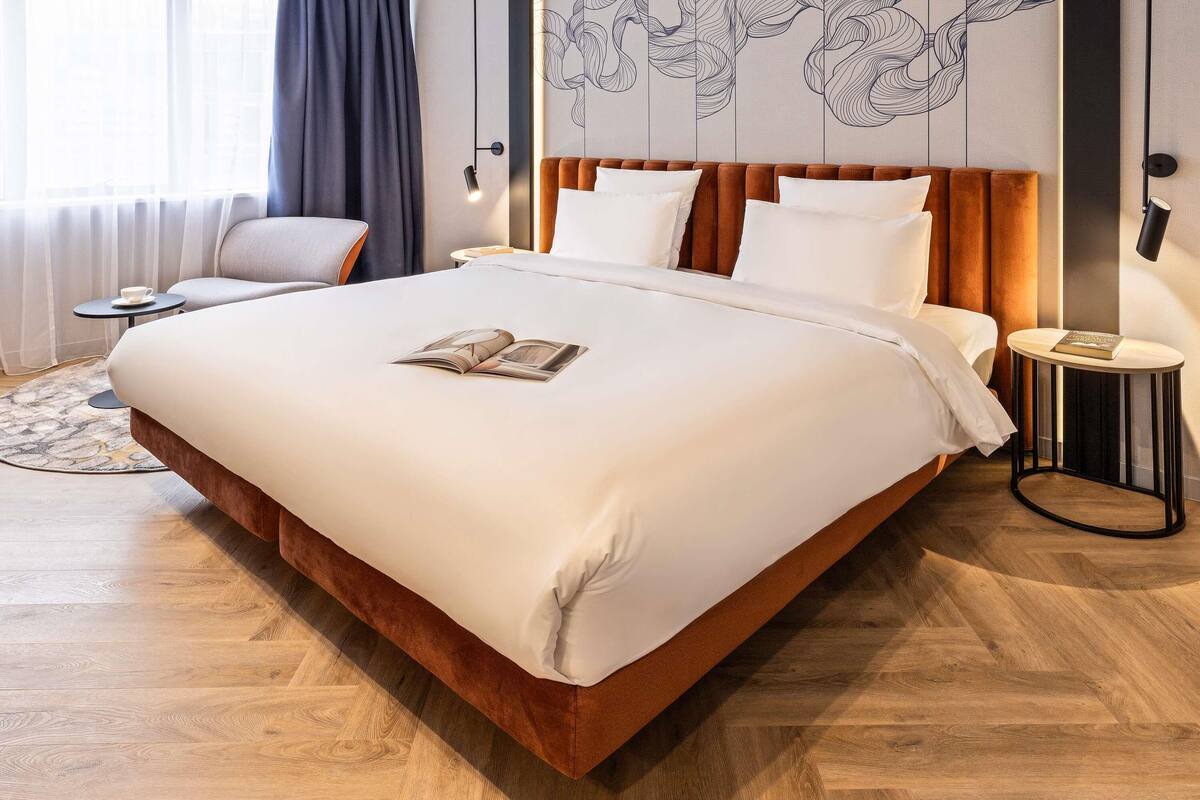 A large bed with a wooden headboard, a bedside table with a book, and a wall with a decorative panel.