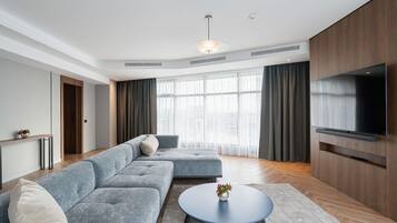 Uma sala de estar moderna com um sofá modular cinza, uma mesa de centro redonda e uma televisão de tela plana fixada em uma parede de madeira.