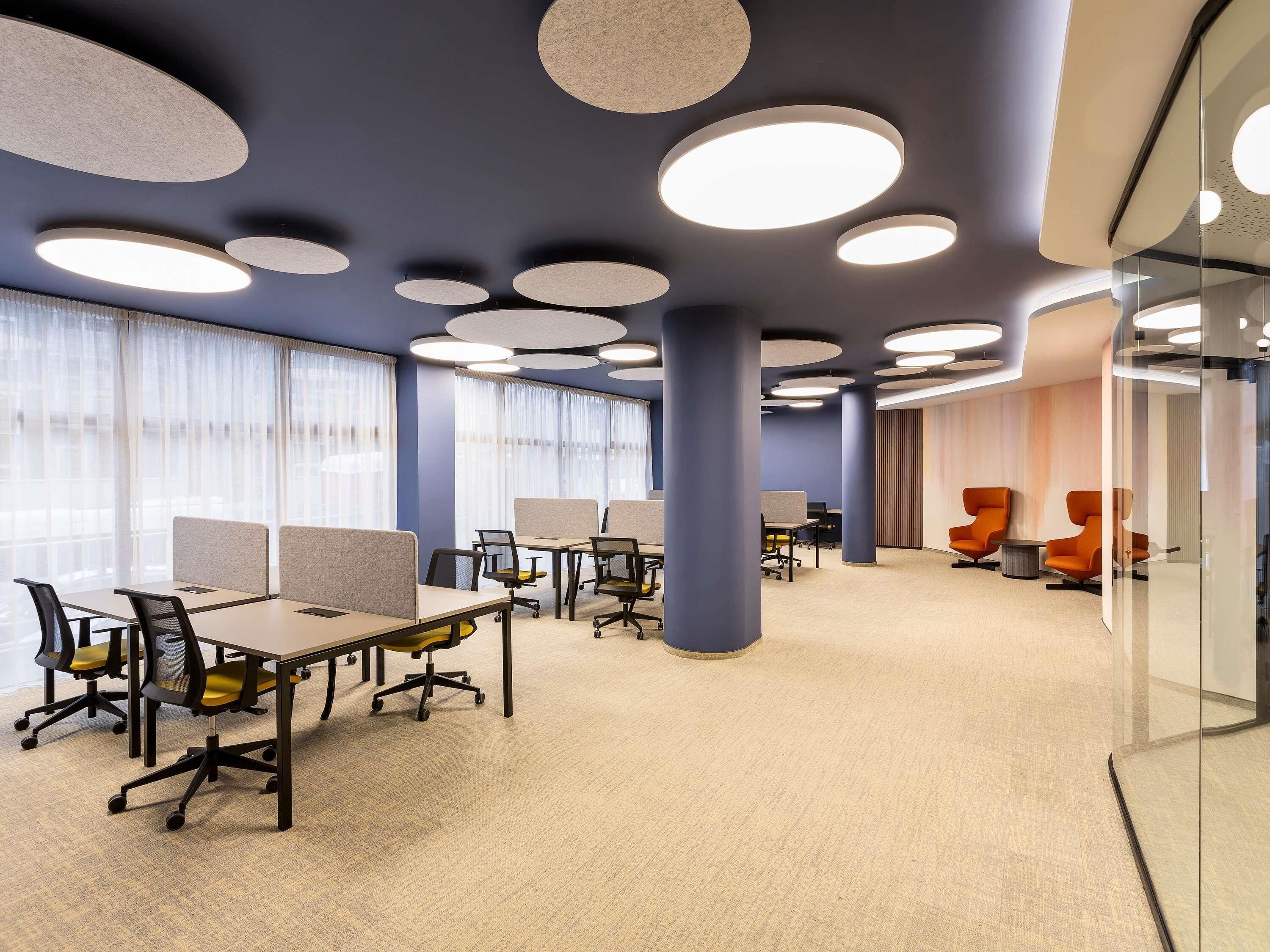 A modern office space with cubicles, ergonomic chairs, and a glass partition wall.