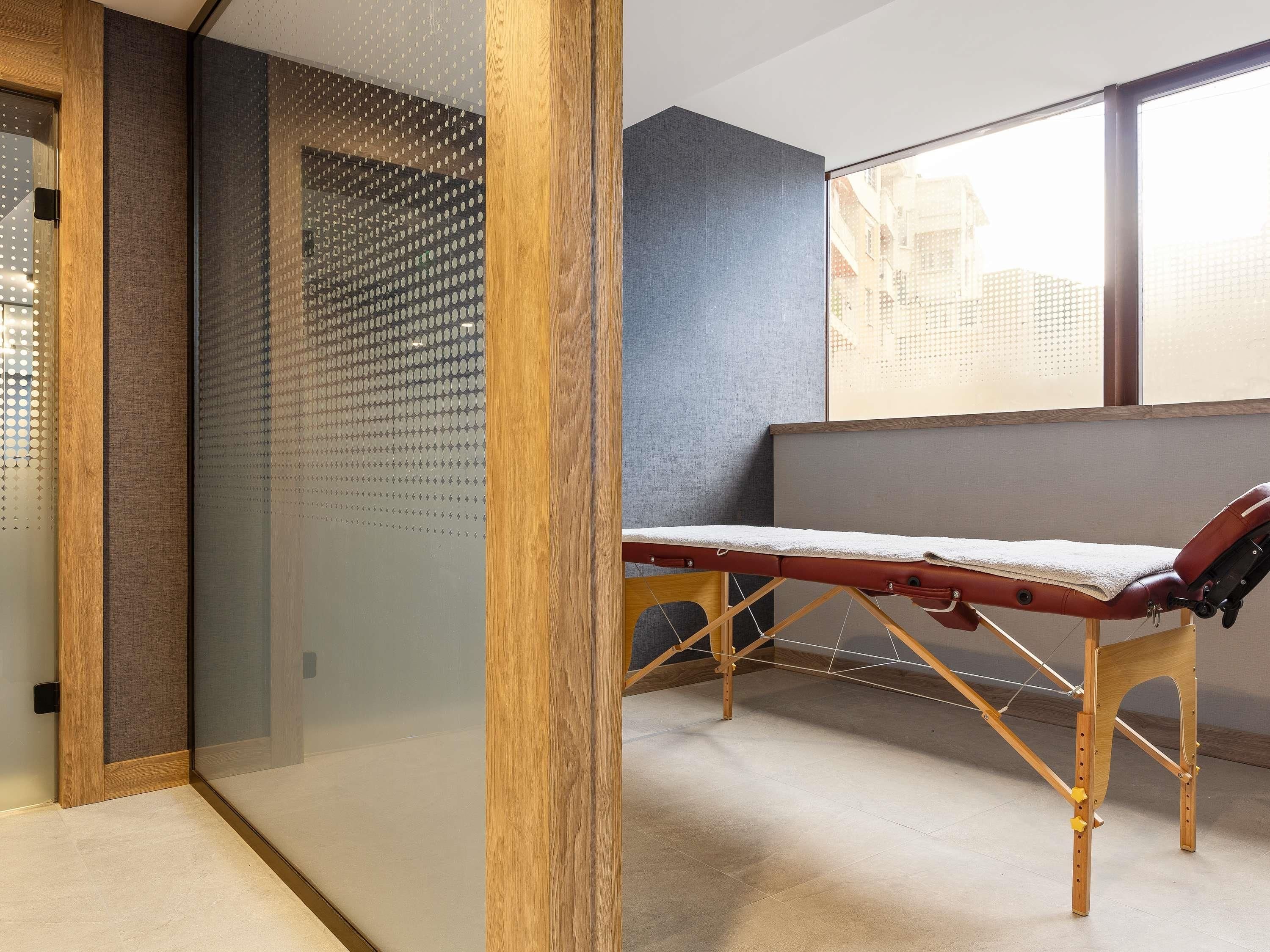 Ein Zimmer mit Massageliege, großem Fenster und Wand mit gelochtem Muster.