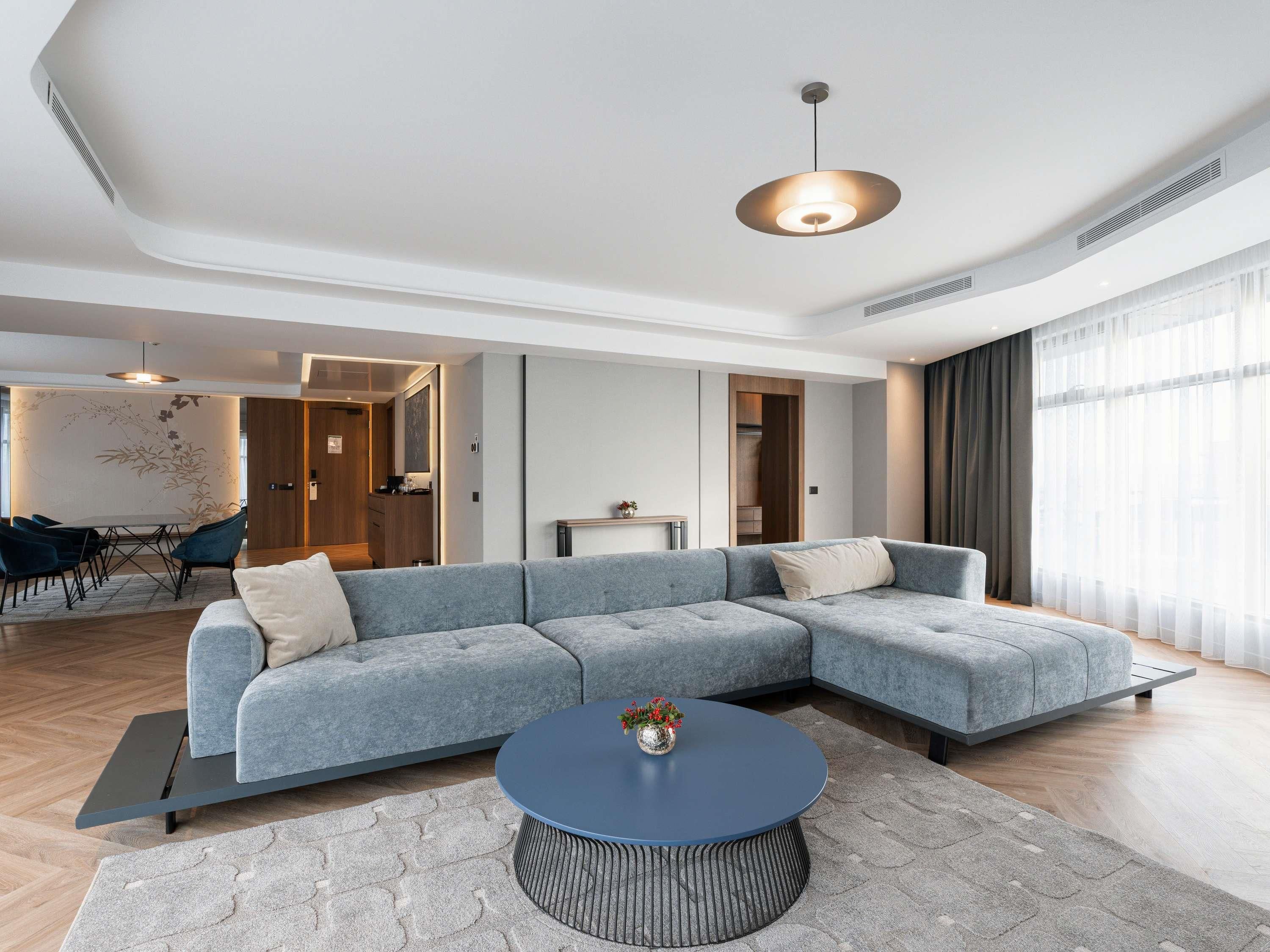 A modern living room with a sectional sofa, a round coffee table, and a dining area with chairs.