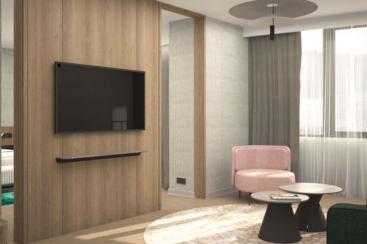 A modern living room with a flat-screen TV mounted on a wooden wall, a pink sofa, a round coffee table, and a green armchair.