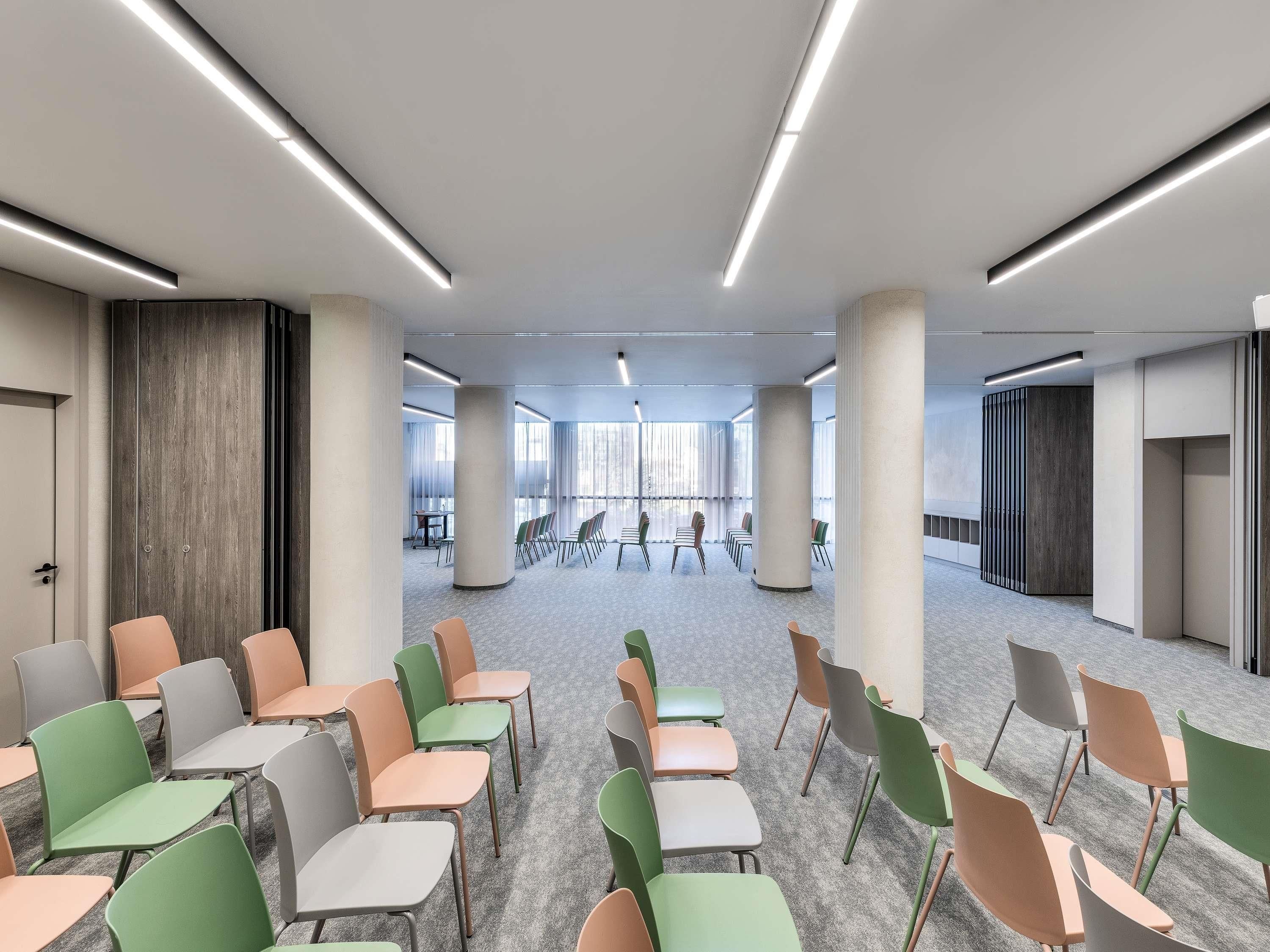 Une salle de conférence avec des rangées de chaises, une longue table et de grandes fenêtres.