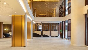 A spacious lobby with a high ceiling, a reception desk, and a staircase leading to an upper level.