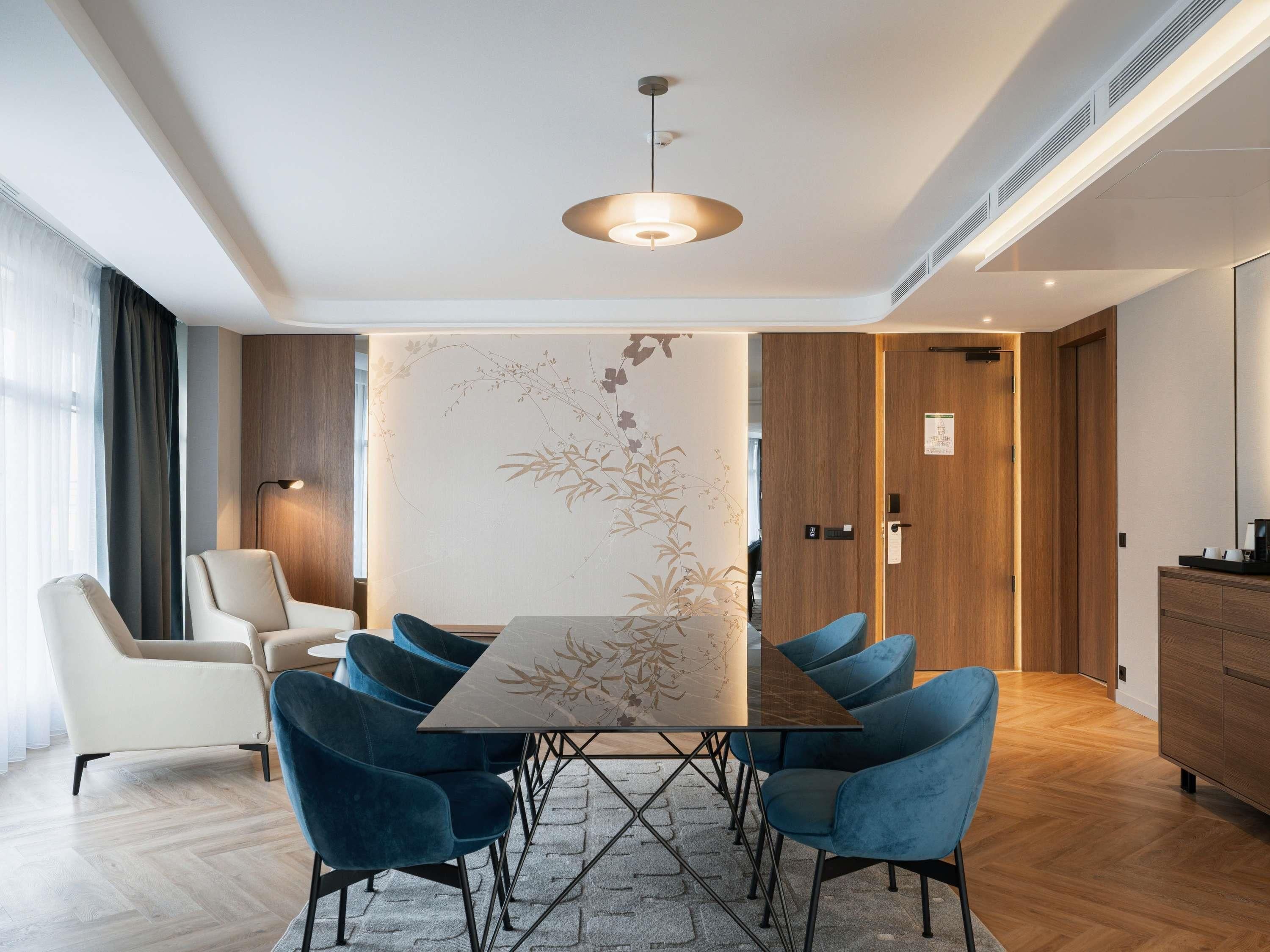 Une salle de conférence moderne avec une table rectangulaire, des chaises rembourrées bleues, un luminaire suspendu et une porte en bois.