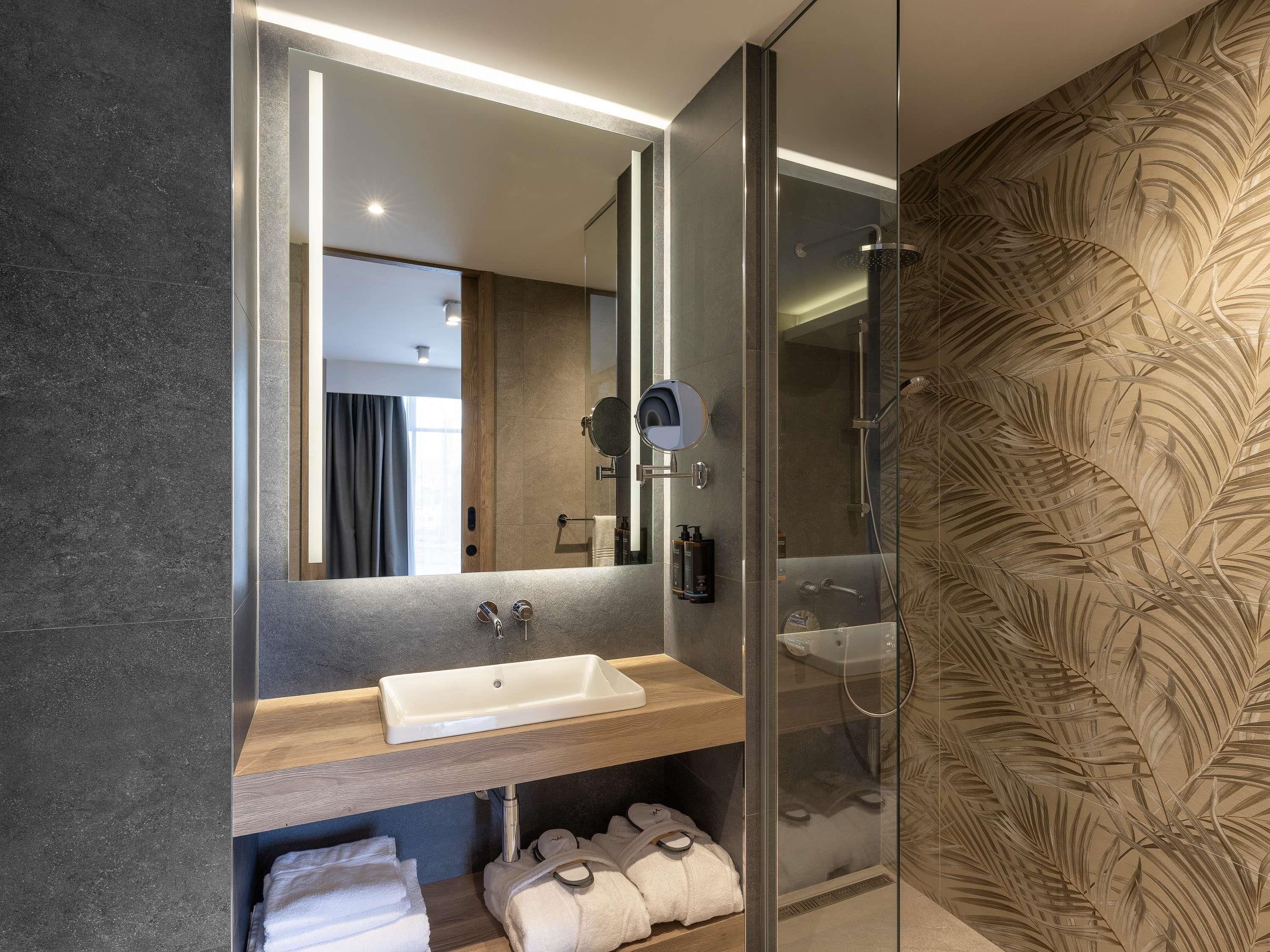 Un baño moderno con ducha envuelta en vidrio, tocador de madera y un espejo grande.