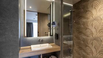 Un baño moderno con ducha envuelta en vidrio, tocador de madera y un espejo grande.