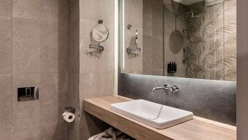 Un baño moderno con un espejo grande, un lavabo blanco, ducha y un perchero para toallas.