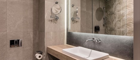 A modern bathroom with a large mirror, a white sink, a shower, and a towel rack.