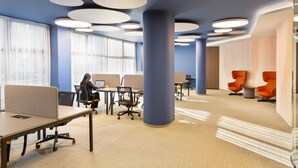 A modern office space with cubicles, a large pillar, and orange chairs.