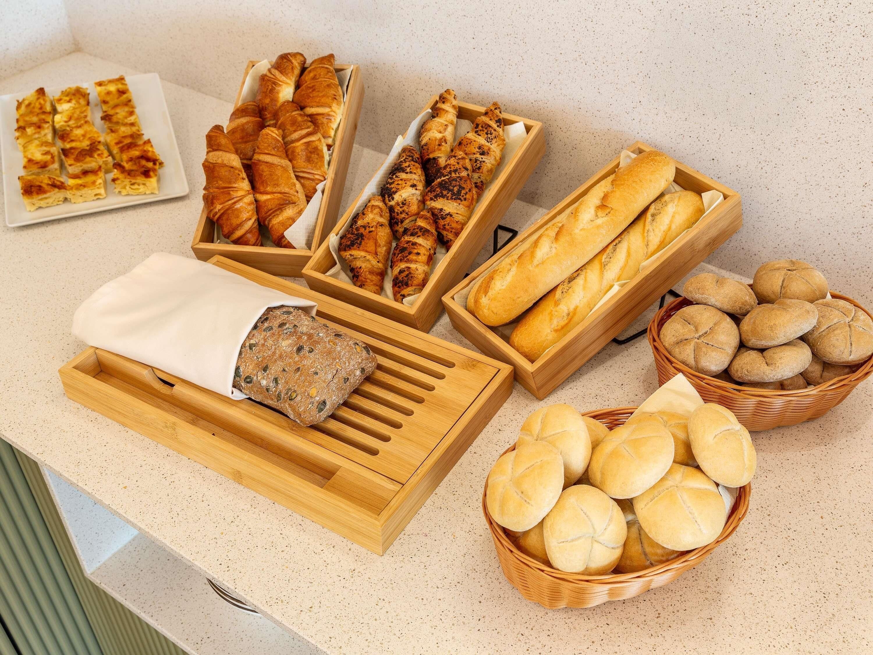 A variety of baked goods including bread, croissants, and rolls displayed in wooden boxes and baskets.