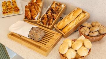 A variety of baked goods including bread, croissants, and rolls displayed in wooden boxes and baskets.